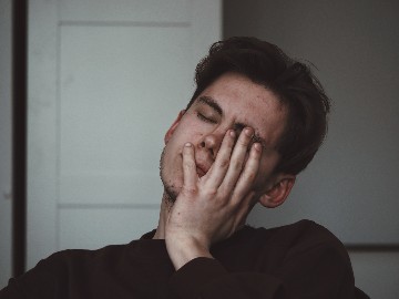 Man met donker haar en zwarte trui heeft pijn in mond door stress.