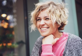 Vrouw met kort blond haar, roze trui en grijs vest is blij met koud door stress tips.