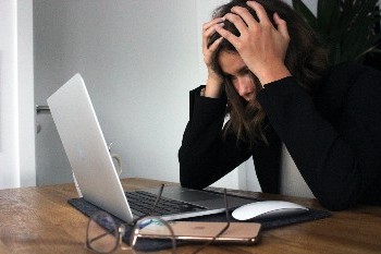 Vrouw met zwart donker haar zit achter computer met handen in het haar door de verwardheid gevolgen werk.